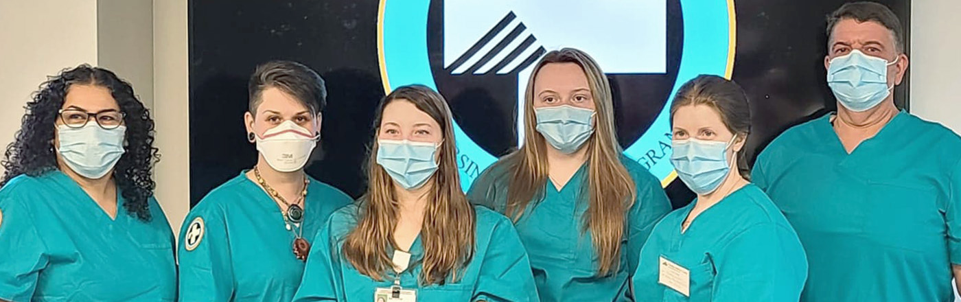  5 young women and one middle aged man wearing masks and matching teal student scrubs pose together for the LNA cohort graduation