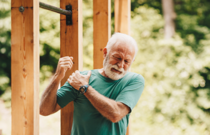 Older man on job site clutches his shoulder in pain as he rotates it upward