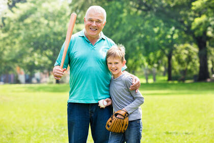 An older man holding a baseball bat with his arm around a child who holds a catcher's mit.