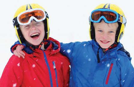 Two kids, standing side-by-side, wearing ski helmets, goggles and winter jackets