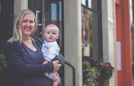 Beth Wood stands on the steps outside her business in downtown Keene holding her baby