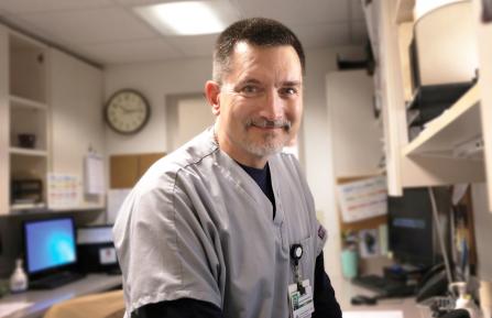 Middle aged man in scrubs pauses to look at camera while using a computer terminal