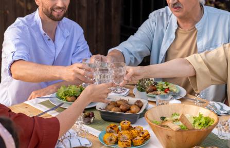People sitting at a table of food, raising glasses in a toast.
