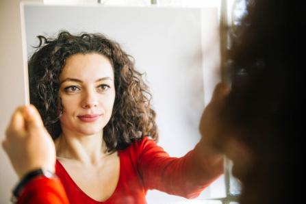 Woman in red shirt holding mirror, looking at her reflection