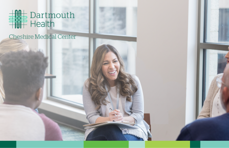 Friendly woman sits talking to group of people. Dartmouth Health Cheshire Medical Center logo