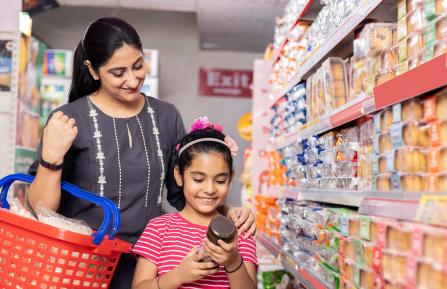 Mother and daughter shop with a basket as a daughter reads the label on a jar