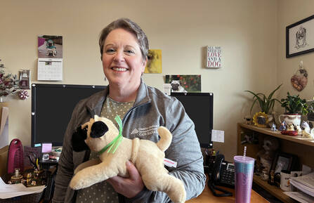 Donna stands in her office full of pug ornaments holding a pug plush toy