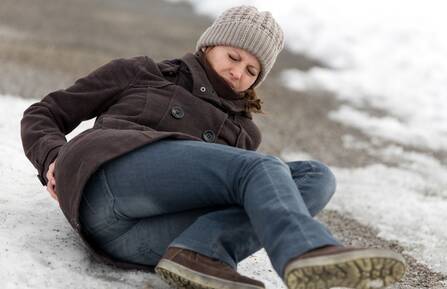 Woman holds tailbone in pain while on the ground, having fallen on ice