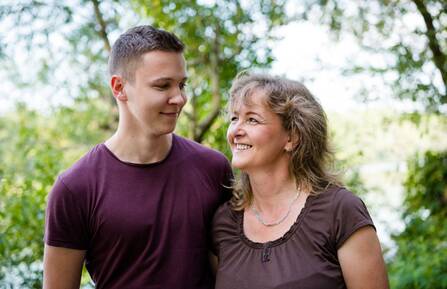 Mother and teenage son look affectionately at each other with an arm around each other.