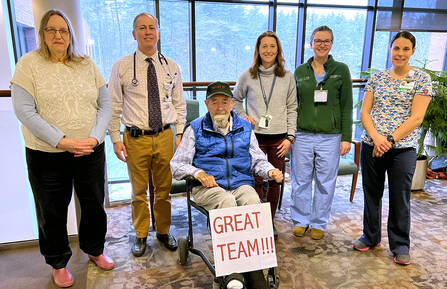 An elderly man in a wheelchair poses with five members of Cheshire Medical Center's clinical staff