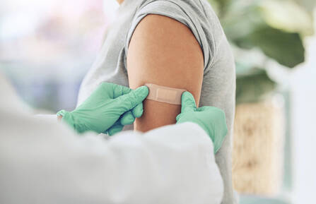 Image of person's arm with a medical professional wearing gloves preparing to administer a flu shot