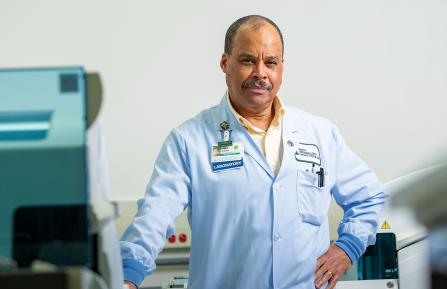 Older man in blue lab coat and badge that reads "Laboratory"