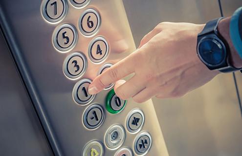 Person's extended finger pushing a button in an elevator