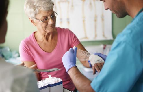 Young provider wraps elderly female patient's wrist with gauze.