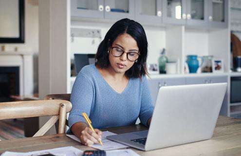 Woman writing while sitting in front of a computer