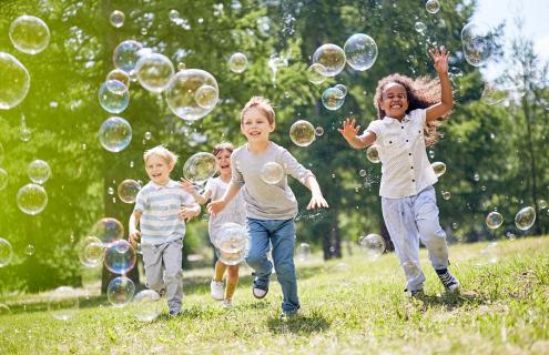 Kids outside, running through bubbles that are floating in the air