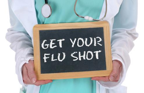 Person holding a slate with the words get your flu shot written on it.