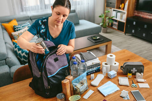 White woman puts items such as water and toiletries into a preparedness kit
