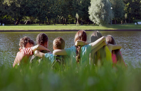 A group of children embrace while looking over a lake