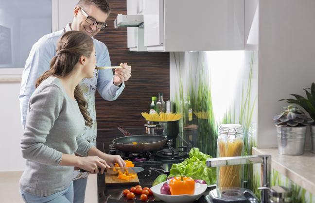 Couple cooking as regular looking guy offers a taste of the dish to a lady