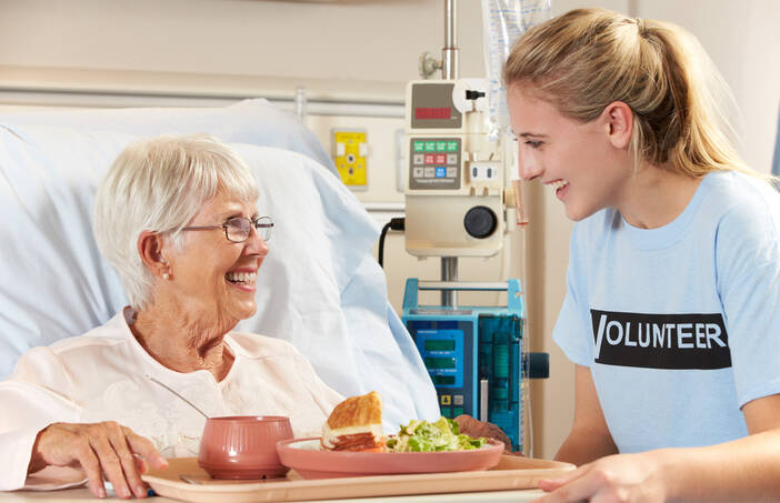 A volunteer speaks with a hospital patient at their bedside